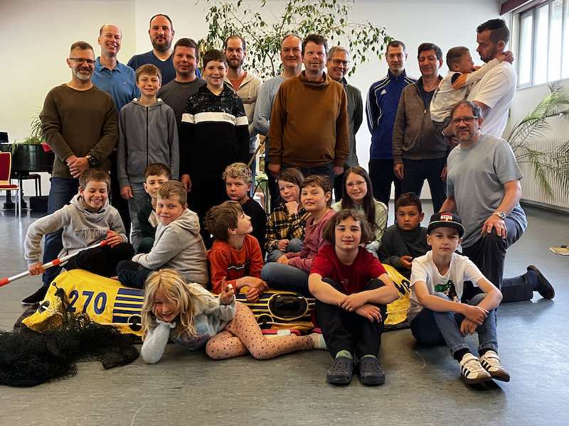 Eine Gruppe mit Vätern und Kindern stehen, sitzen oder liegen in einem Raum.