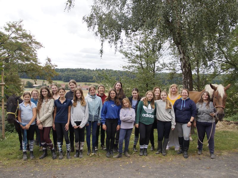 Eine Gruppe von Mädchen steht in einer Reihe, rechts und links ist jeweils ein Pferd.