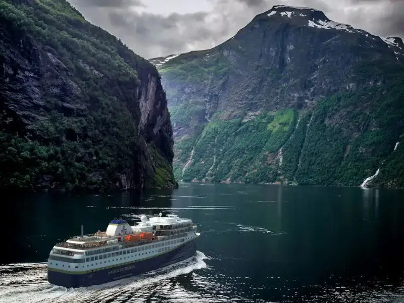 Ein großes Schiff durchquert einen norwegischen Fjord, der von Bergen gesäumt ist.